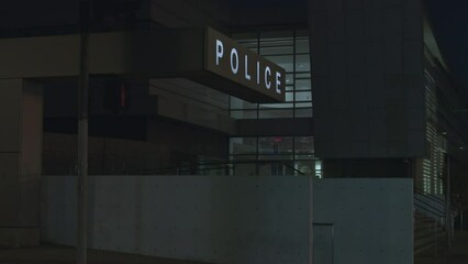 Car headlights lighting up the walls of a police station at night. Entrance of the police department with dark building as background