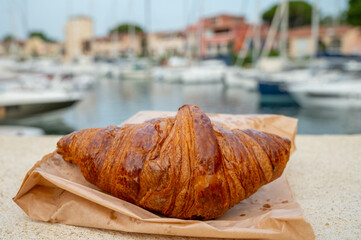 Fresh baked french croissant and boats of Port Grimaud on background, south of France