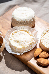 French cheeses Rocamadour and Saint-Marcellin served on olive tree wooden plank with almonds