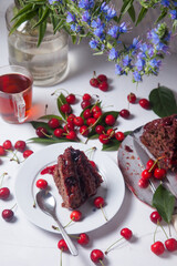Chocolate cake with sweet cherry, cup of tea and bouquet of blue flowers on white background..