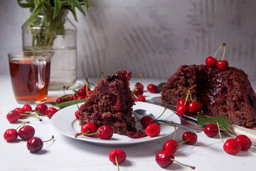 Chocolate cake with sweet cherry, cup of tea and bouquet of blue flowers on white background..