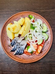 large vertical photo. homemade food. boiled potatoes with pieces of salted mackerel and vegetable salad on a brown clay plate. eco. bio.
