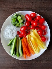 large white plate with chopped vegetables and sauce. slices of pepper, carrot, cucumber and tomato for appetizer. healthy vitamin food. eco. bio. seasonal vegetables. mix of vegetables for the diet.