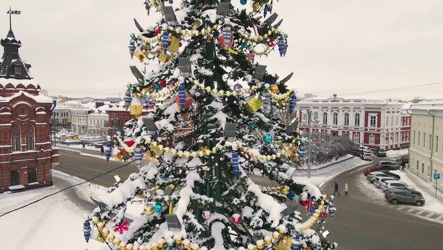 Festive toys and golden garlands on the Christmas tree, aerial view. New Year's, green spruce fabulously decorated and covered with snow. City of Vladimir, Cathedral Square, Russia. UHD 4K.