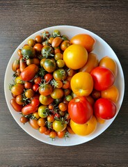 large vertical photo. large round plate with cherry tomatoes and yellow tomatoes. view from above. healthy vegetables. home garden. eco. bio.