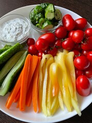large vertical photo. close-up on a plate with different vegetables. diet food. beautiful summer seasonal vegetables. carrot. mini tomato and cucumbers on a white plate. eco. bio.