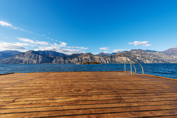 Wooden pier on the coast of Lake Garda (Lago di Garda) and Italian Alps view from the small town of Malcesine, Verona province, Italy, Veneto, southern Europe. On background the coast of Lombardy. 