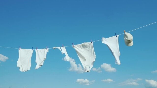 White clothes and a children's cap are drying on a clothesline against a blue sky