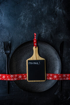 Overhead view of a blank individual menu blackboard on a plate with a festive Christmas ribbon