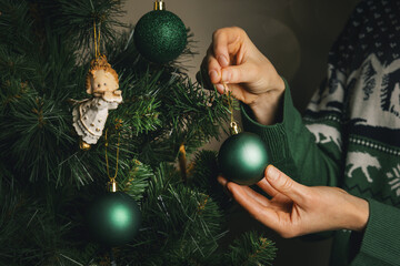 decorating a christmas tree. closeup of female hands hang a green ball on a branch