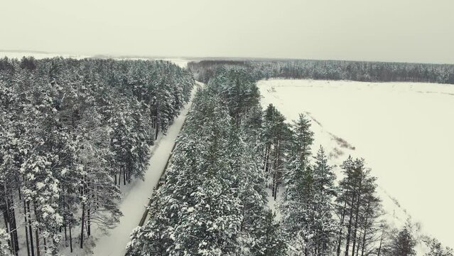 Aerial view of a narrow country road in winter, snow all around. Woodland and field. Central Russia. Fabulous winter natural landscape, background, screensaver, footage, video. UHD 4K.