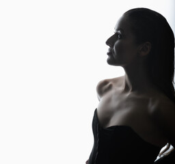 Portrait of beautiful and sexy brunette woman silhouette with black corset and wet hair in glowing studio background. Model standing in grace pose and looking aside camera with seductive look