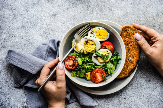 Overhead View Of A Woman Eating A Salad With Hard Boiled Eggs, Avocado, Tomato, Lettuce And A Slice Of Toast