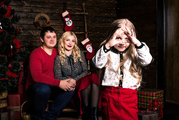 Beautiful young family in red having fun together for Christmas holidays, sitting on a living room floor next to a nicely decorated Christmas tree