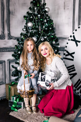 Fototapeta na wymiar Mother and daughter gathering together near the christmas tree. The clock in the background show five minutes to midnight. Christmas Eve. New Year. Holiday and fun. Merry Christmas.