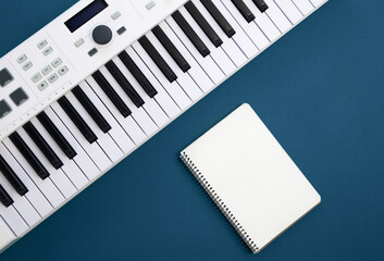 Fototapeta na wymiar Piano keys and blank notepad on blue background, flat lay.