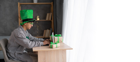 Young man working on the laptop with gifts on St.Patrick's Day. Patrick's Day shopping online,...