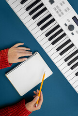 Female hands, empty notepad and music keys on green background, flat lay.