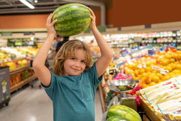 Fototapeta premium Kid with watermelon. Funny cute child on shopping in supermarket. Grocery store. Grocery shopping, healthy lifestyle concept.