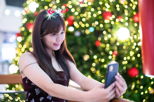 Portrait young asian woman red dress costume Take a selfie with a smartphone and picture parcel decoration on Christmas tree light circular bokeh background Decoration During Christmas and New Year.