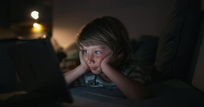Close up of boy 4-5 years child while using a tablet Concept, kid dream online video games at night concept. caucasian boy watching online video, digital tablet network. child on social media