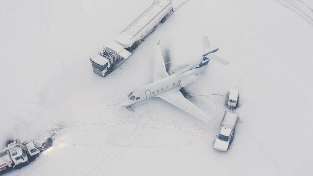 Embraer business jet on snowy tarmac with support vehicles, aerial