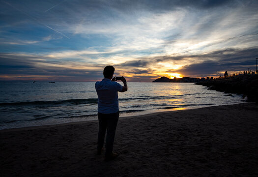 Hombre haciendo una foto con su smartphone al paisaje del atardecer que se le presenta en Benidorm en un viaje de trabajo.