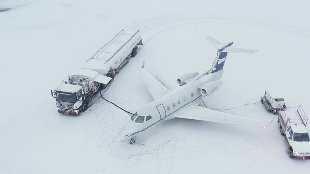 Fuel truck refueling private Embraer jet in snowy conditions, aerial