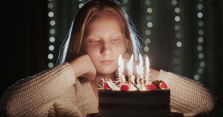A slightly sad teenage girl looks at the candles on her birthday cake.