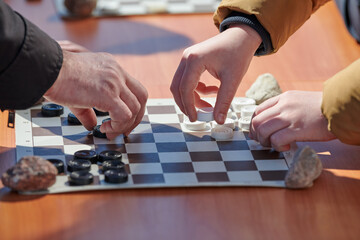 Outdoor checkers tournament on paper checkerboard on table, close up players hands. Outdoor...