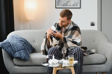 A sick man sits at home on a gray sofa with a blanket. Illness, protection, coronavirus, illness, flu