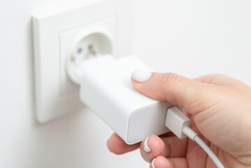 Female hand inserts charging device into electrical outlet, close up. Consumption of electricity, getting power to mobile phone to stay in touch with the world