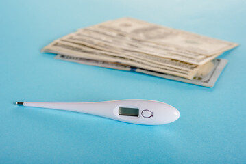 Electronic thermometer and hundred dollar banknotes on blue background
