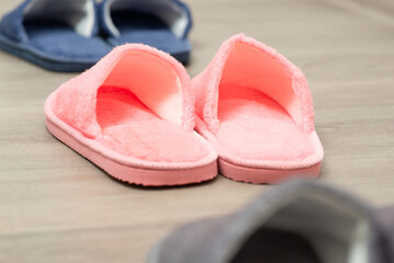Home warm slippers standing in a row on the floor, close up. Focus on pink footwear on house parquet indoors