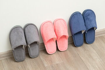 Three pairs of new home slippers stand on the grey floor near white wall. Cozy comfortable footwear for cold periods