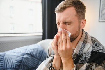 Sick man on sofa at home and blowing nose