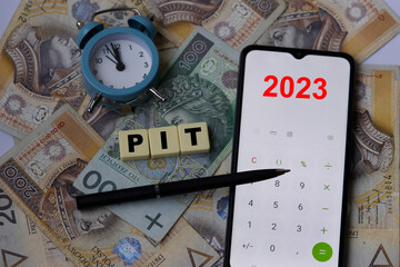 Concept for financial reminder to pay income tax in 2023. Polish money. Single hundred banknote on two hundred polish zloty background. Clock, pen and mobile phone calculator. Inscription PIT.