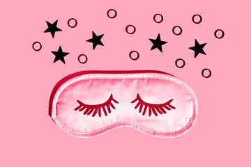 Pink sleep mask with eyelashes on a gray background with black stars. Healthy sleep concept. Space for text,top view. Demonstrating the colors of 2023 Viva Magenta.
