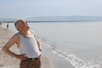 Un signore anziano vestito in canottiera  in riva al mare si gode il sole estivo 