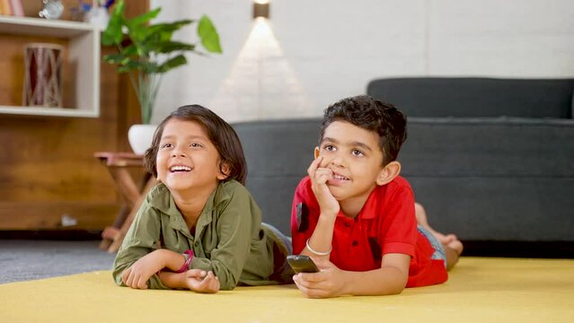 Happy smiling teeanger siblings watching tv or television while laying on floor at home - concept of enternatimnnet, bonding and weekend holidays