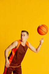 Portrait of young emotive man in orange uniform playing basketball, training, spinning ball on...