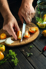Preservation of vegetables in a jar with aromatic spices. The cook cuts tomatoes on a kitchen cutting board. Peasant food