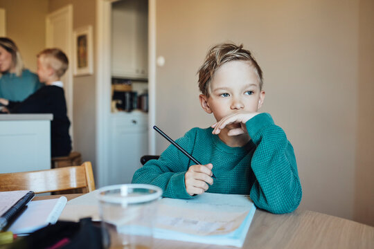 Thoughtful boy with pencil and book sitting at table