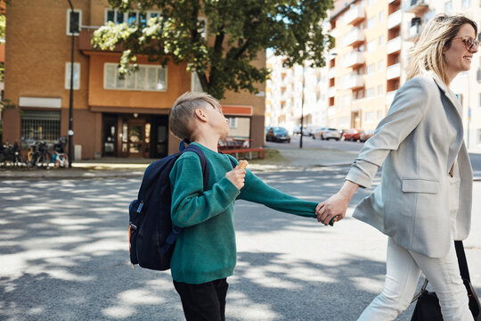 Side view of woman taking stubborn son to school while walking on street