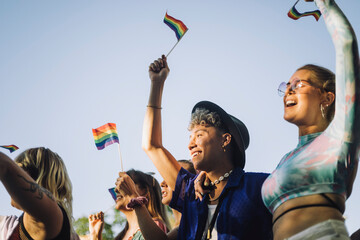 Happy man and woman with hands raised holding rainbow flags while enjoying in gay pride parade