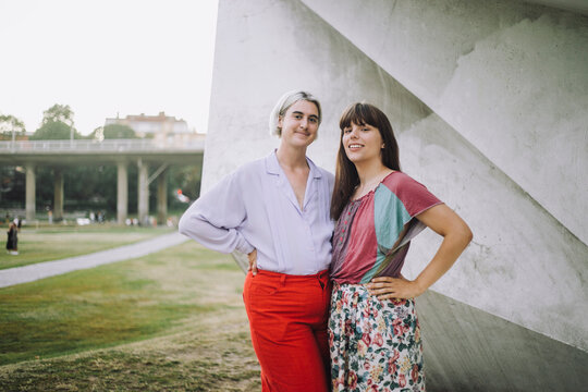 Portrait of smiling non-binary person and woman standing with hands on hips at park