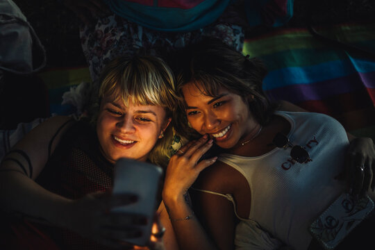 Happy non-binary person taking selfie with female friend through smart phone