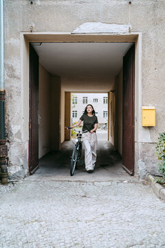 Woman wheeling with bicycle while walking out of archival doorway