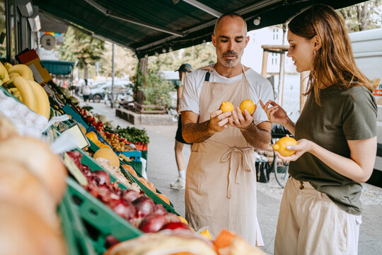 Male vendor wearing apron while assisting female customer buying lemons at market