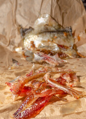 Selective focus on pieces of oily dried salted fish on crumpled craft paper.